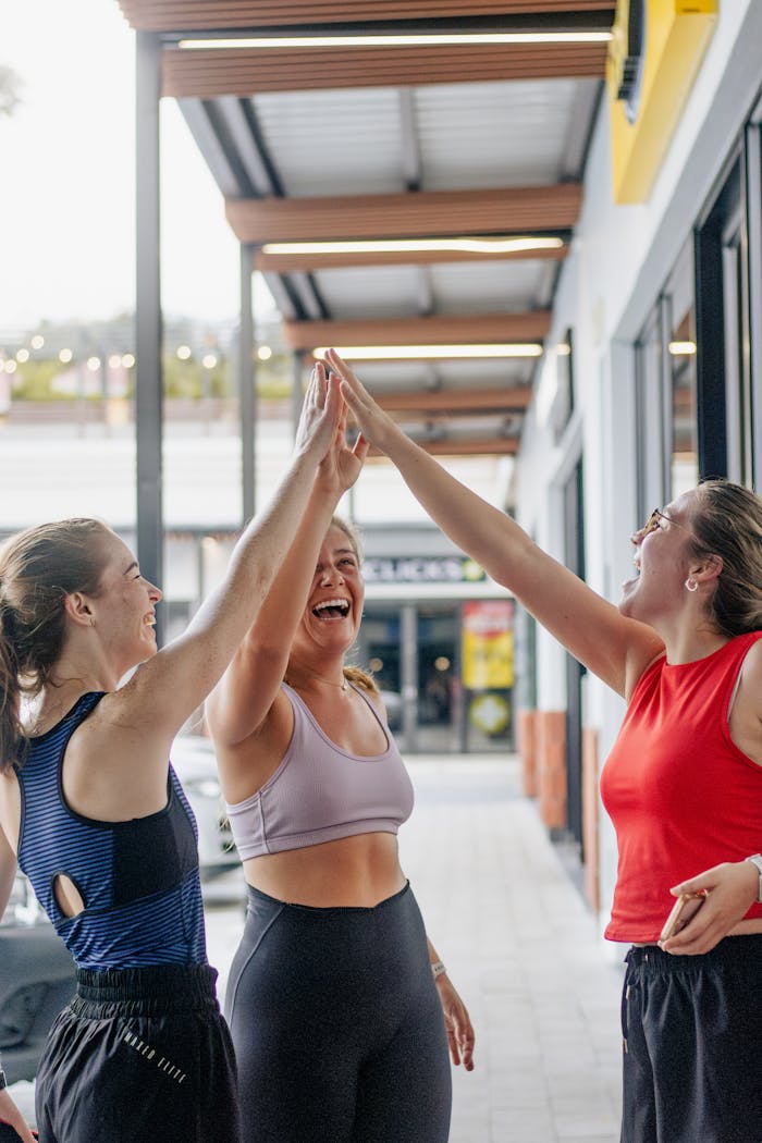 Three women celebrating success and friendship with high-fives outdoors.